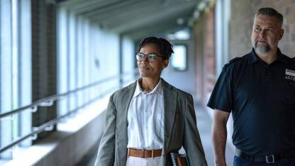 Zwei Personen gehen durch einen Flur, eine trägt ein Namensschild mit 